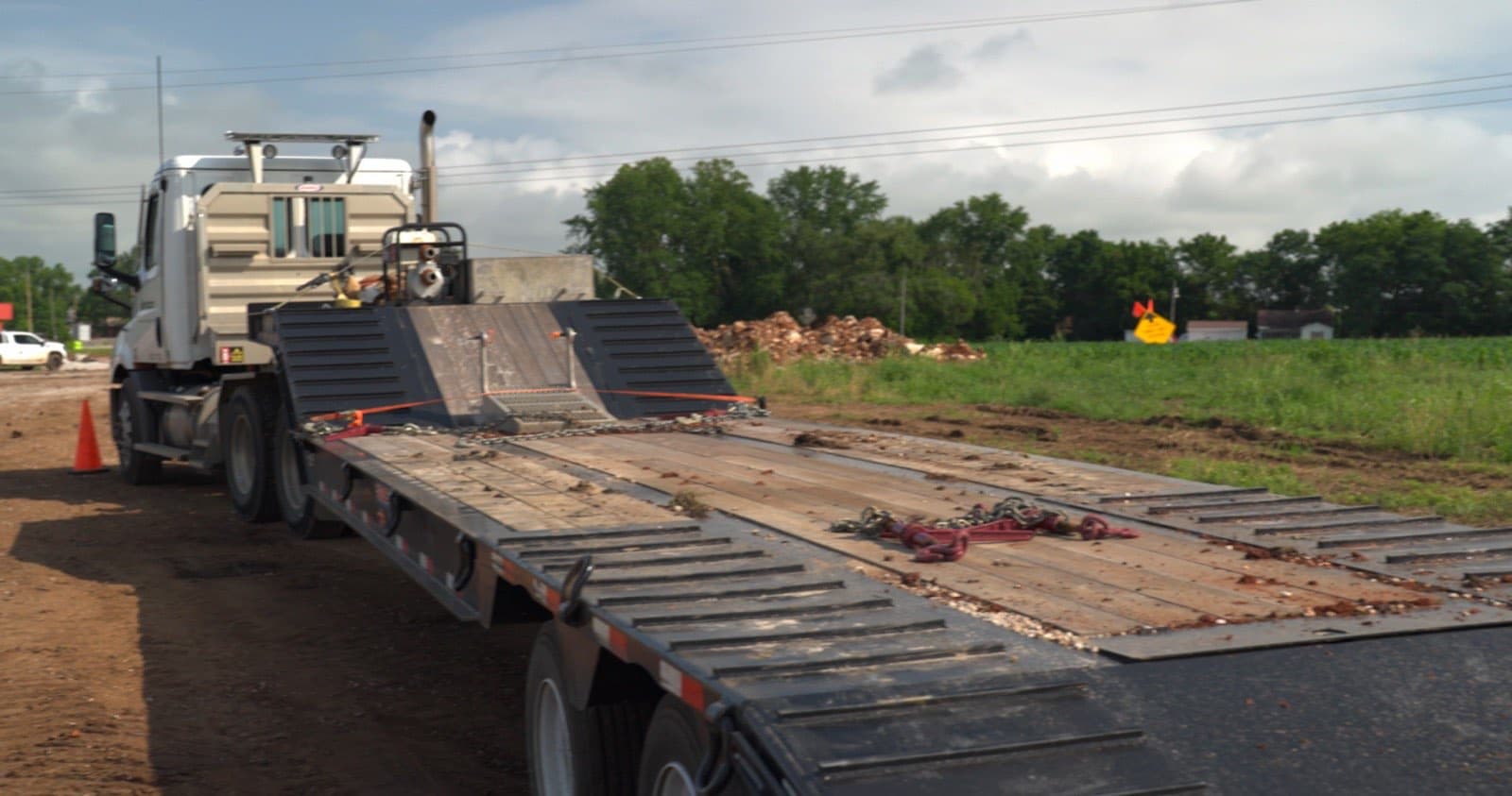 An empty step deck behind a white Peterbilt with chains and binders staged on the wooden deck